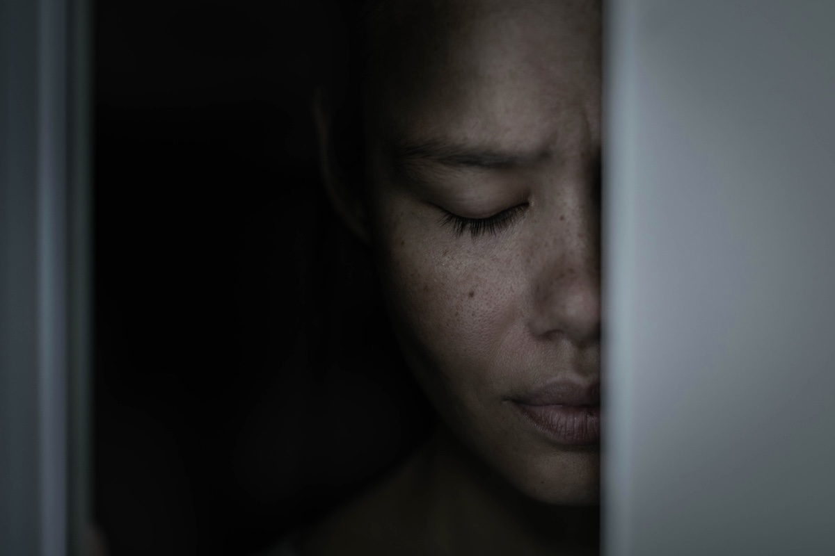 A scared woman depressed pressing face against door and frightened.